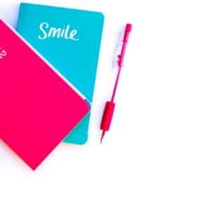 Colorful flat lay with turquoise and pink notebooks and matching pen on white background.